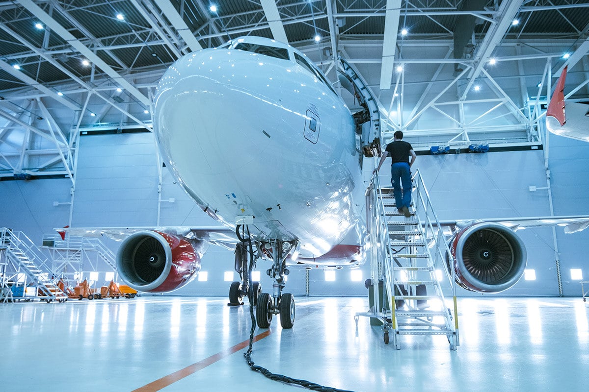 Ein Flugzeug steht in einem Hangar, während ein Arbeiter mit Wartungs- und Vorbereitungsarbeiten beschäftigt ist