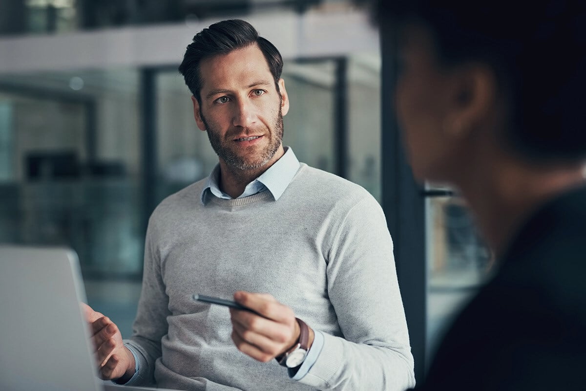 Zwei Männer führen ein Gespräch in einem Büro. Der Austausch wirkt professionell und konzentriert